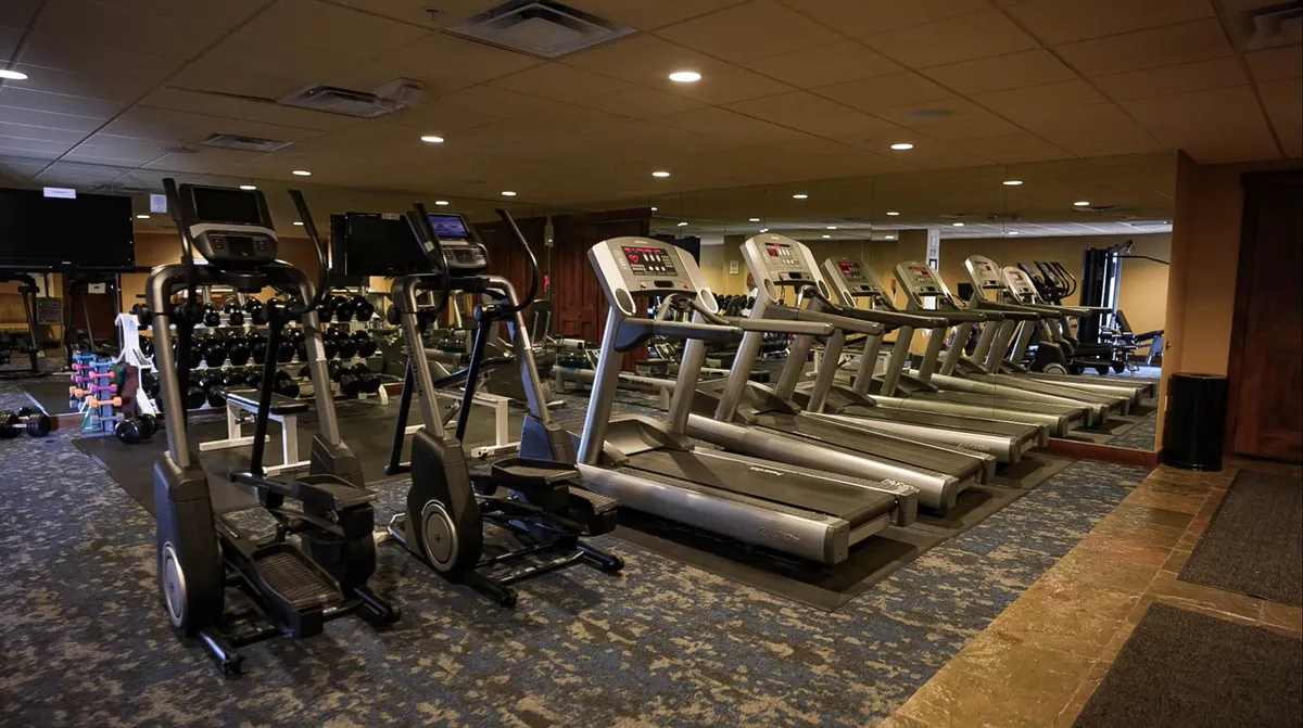 An interior fitness center with treadmills, elliptical machines, free weights, and a mirrored wall. The space is bright and modern, designed to motivate guests for workouts or group fitness activities.