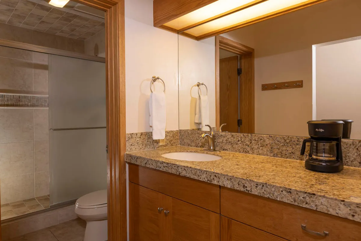 A well-appointed bathroom interior with a granite countertop, modern sink, coffee maker, and a glimpse of the shower area. The atmosphere is relaxed and inviting, ideal for morning routines or unwinding after a day outdoors.