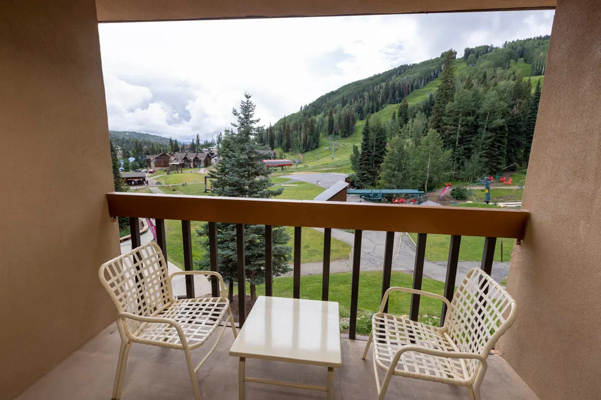 A peaceful exterior balcony with comfortable chairs and a small table overlooks the dramatic Needles Mountain Range. The scene is bathed in natural light and invites travelers to relax while taking in the breathtaking mountain views. The ambiance is tranquil, suggesting a perfect spot to unwind after a day of adventure.